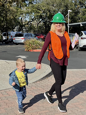 teacher wearing a hard hat and safety vests walks hand in hand with a child