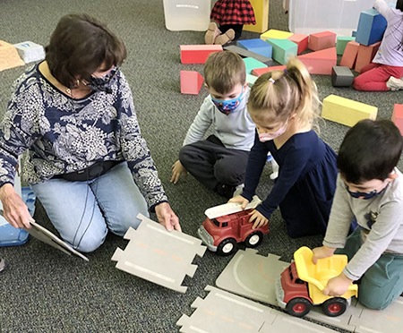 children and teacher on the floor playing with trucks