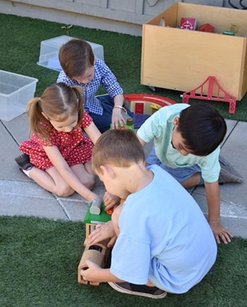 four children playing outside with a train set